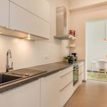 Moderne Küche mit Arbeitsplatte, Spüle und Dunstabzug. Durchgang zur Essnische mit Tisch und Stühlen.