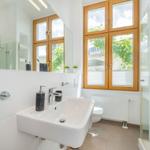 Badezimmer mit Waschbecken, Dusche und Fenster mit Holzrahmen.