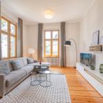 Wohnzimmer mit Sofa, TV und Holzboden. Fenster mit Vorhängen und Beleuchtung.