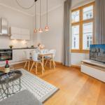 Wohnung mit Küche, Esstisch und Fernseher. Holzboden und großes Fenster.