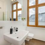 Badezimmer mit Waschbecken, Toilette und Dusche. Große Fenster mit Holzrahmen.