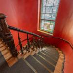 Elegante Treppe mit Holzgeländer und farbigem Glasfenster an roter Wand.