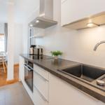 Moderne Küche mit Arbeitsplatte, Spüle und Dunstabzug. Im Hintergrund ist Essbereich mit Tisch und Stühlen.