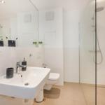 Badezimmer mit Dusche, Waschbecken und Toilette. Weiße Fliesen und Spiegel.