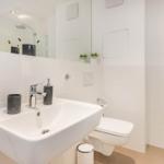 Badezimmer mit Waschbecken, Toilette und Dusche. Weiße Fliesen und Spiegel.