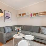 Ein Wohnzimmer mit grauem Sofa, weißen Regalen und einem Stehlampe.