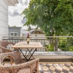 Balcony with wicker chairs, table, and wine bottle. View of trees and buildings.