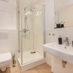 Badezimmer mit Dusche, Waschbecken und Toilette. Weiße Fliesen und moderne Armaturen.