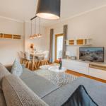 Wohn- und Essbereich mit Sofa, TV und Esstisch. Holzboden und helle Wände.