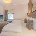 Schlafzimmer mit Doppelbett, Wandbild und Fenster mit Blick auf Gebäude.