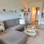 Wohnzimmer mit grauem Sofa, Glas-Tisch und Küchenbereich im Hintergrund.