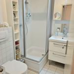 Badezimmer mit Dusche, Waschbecken und Toilette. Weiße Fliesen und Regale.