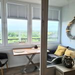 Sitzbereich mit Tisch und Sitzgelegenheiten, Blick auf Landschaft durch Fenster.