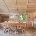 Essbereich mit Holztisch, Stühlen und Fenstern. Holzwände und -decke. Barhocker an der Wand.