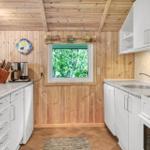 Küche mit Holzwänden, Fenster mit Blick auf Bäume, weißen Schränken und Arbeitsplatte.