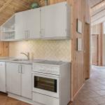 Küche mit weißen Schränken, Spüle, Herd und Backofen. Holzwände und Fliesenboden.