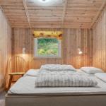 Schlafzimmer mit Holzwänden, Bett, Stuhl und Fenster mit Blick auf Grün.