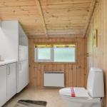 Badezimmer mit Holzwand, Toilette, Waschbecken und Fenster mit Gitter.