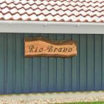 Holzschild mit der Aufschrift Rio Bravo an einer blauen Hauswand unter einem Ziegeldach.