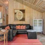 Wohnzimmer mit schwarzer Couch, rotem Teppich und Holzwand. Küche im Hintergrund.