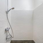 Dusche mit Handbrause und Ablagekorb an weißer Wand