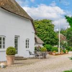 Weißes Haus mit Strohdach, Terrasse und Garten. Holztisch, Stühle, Pflanzen.