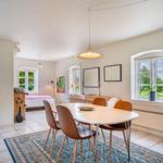 Essbereich mit Tisch und Stühlen auf Teppich. Im Hintergrund Schlafzimmer und Fenster mit Blick auf Garten.