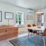 Esszimmer mit Tisch, Stühlen und Holzschrank. Blauer Teppich und Fenster mit Pflanze.