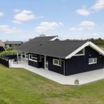 Ein schwarzes Ferienhaus mit weißem Holzdeck und Garten. Hintergrund: Gras und Bäume.