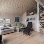 Wohnzimmer mit Sofa, Sessel und Spiralrampe. Holzwände und Boden. Kamin und Fenster.