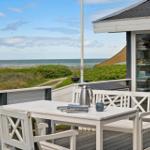 Terrasse mit weißem Tisch und Stühlen, Blick auf Strand und Meer.