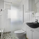 Badezimmer mit Toilette, Dusche und Waschbecken. Weiße Holzwandverkleidung und Mosaikfliesenboden.