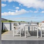 Terrasse mit weißem Tisch und Stühlen, Blick auf Strand und Himmel.