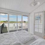 Schlafzimmer mit Blick auf Terrasse und Strand. Weißes Bett, weiße Wände und Holzboden.