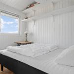 Schlafzimmer mit weißer Holzwand, Bett und Fenster zum Himmel.