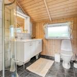 Badezimmer mit Dusche, Waschbecken und Toilette. Holzwände und Fenster mit Vorhängen.