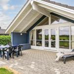 Terrasse mit Tisch, Stühlen und Liegestuhl vor einem Haus mit Glasfront.