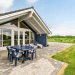Haus mit Terrasse, Tisch und Stühlen. Grünflächen und Wald im Hintergrund.