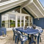 Terrasse mit blauem Tisch und Stühlen, Glasfront und Grill. Grün hinter dem Haus.