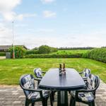 Terrasse mit Tisch und Stühlen. Grünfläche und Hecke im Hintergrund.