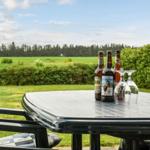 Außenbereich mit Tisch, Stühlen und Bierflaschen vor grünem Feld und Hecken.
