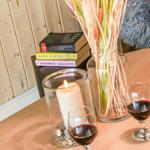 Tisch mit zwei Weingläsern, Kerze und Blumenstrauß. Bücher stapeln sich im Hintergrund.