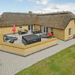 Haus mit Strohdach, Terrasse mit Liegen und Grillplatz, umgeben von Grünfläche.