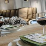 Tisch gedeckt mit Weingläsern und Teller. Im Hintergrund Sofa mit Felldecke.
