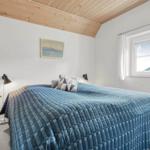 Schlafzimmer mit Bett, blauer Decke, Fenster und Holzdecke.