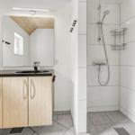 Bad mit Dusche, Waschbecken und Spiegelschrank. Weiße Fliesen und Holzoberflächen.