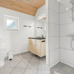 Badezimmer mit Dusche, Waschbecken und Toilette. Holzdecke und Fenster sichtbar.