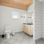 Badezimmer mit Toilette, Waschbecken und Dusche. Holzdecke und weiße Fliesen.