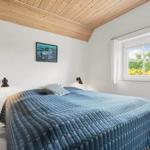 Schlafzimmer mit Bett, Wandbild und Fenster. Holzdecke und weiße Wände.