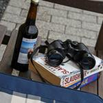 Eine Flasche Bier, ein Fernglas und Bücher auf einer Holzbank.